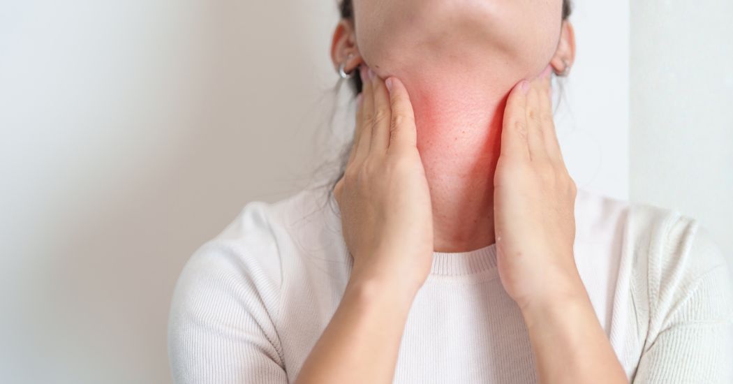 Γυναίκα αγγίζει τον λαιμό της με ερυθρότητα στην περιοχή του θυρεοειδούς, χασιμότο συμπτώματα.